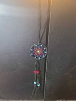 Full view of dreamcatcher pendant necklace hanging, showing cord and tassels