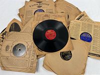 Stack of 78 RPM records in various company sleeves, one disc displayed