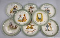All eight Holly Hobbie plates laid out to show variety of illustrations and matching green rims
