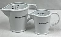 Both ceramic measuring pitchers side by side showing size difference and exterior graphics