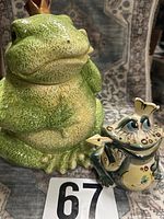 Large green ceramic frog prince cookie jar and smaller hand-painted frog tea jar side by side