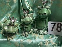 Group shot of three green ceramic frog figurines with silver crowns