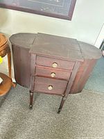 Front view of dark mahogany sewing cabinet showing drawers, glass knobs, turned legs
