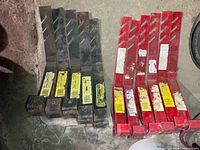 Group of twelve adjustable steel roof jacks, six red and six black, showing overall condition