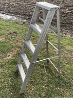 Side view of aluminum 4-step A-frame ladder on grass