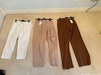 All three pairs of pants laid flat on hangers: white, beige, brown