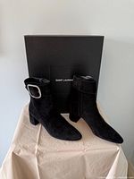 Pair of black suede Saint Laurent ankle boots in front of branded box