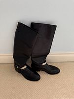 Side view of tall black leather boots leaning against wall