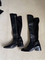 Full view of both boots laying flat showing leather fronts, stretch panels, zippers, and heels