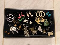 Black tray holding assorted costume earrings, various colours and shapes