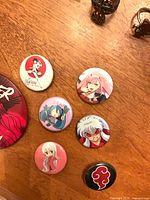 Group of six anime pins on wood surface