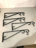 Four identical black metal wall brackets laid out side by side