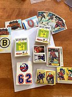 Stacks of stickers including team logos (Boston Bruins, New York Islanders), Slap-Shot Game cards, player stickers and holographic inserts