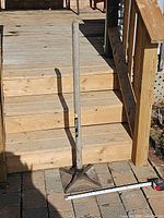 Full view of plate tamper leaning against stairs showing entire handle and square head