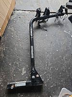 Full view of black steel 3-bike hitch rack showing receiver mount, support arm, three cradle sets, straps, and general wear