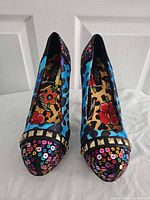 Front view of both shoes showing blue leopard print, sequin toe caps, gold stud band, floral lining