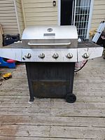 Front view of Master Forge grill showing five control knobs, stainless lid, black lower cabinet, one wheel