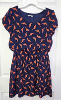 Front view of navy dress with orange dinosaur print displayed on hanger