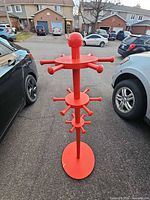 Full view of red wooden coat and hat rack showing base, central pole, tiered hooks and top finial