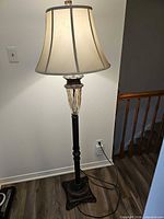 Full view of traditional black metal floor lamp with beige fabric shade and glass accent