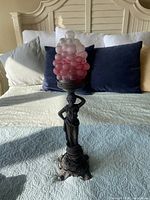 Full view of bronze-finish female figure lamp with frosted grape shade on bed background