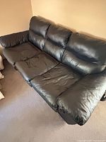 Front angle of black faux leather sofa showing seating area and cushions