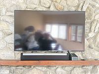 Front view of wall-mounted flat-screen TV with Sonos soundbar and accessory organizer visible on shelf