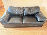 Front view of black bonded leather loveseat showing overall design and cushions