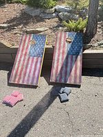 Two cornhole boards and four visible bean bags on pavement