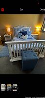 Fully assembled white queen bed frame with bedding, lamps on side tables, blue ottoman at foot
