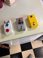 Three DIY guitar pedals lined up: white, aluminium, yellow