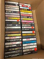 Open box with three vertical stacks of cassette albums showing titles, artists and case condition