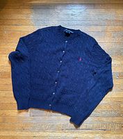Front view of navy cable-knit cardigan showing buttons, pockets, logo