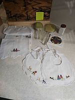 Group view of vanity set, milk glass jar, stained glass tile, embroidered linens and bibs