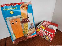 Front view of Fisher-Price #610 measuring toy on card alongside boxed Musical Camera Kaleidoscope