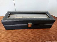 Closed black watch box showing exterior, glass top, clasp, stitching