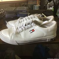 Side view of both white sneakers showing flag logo and sole design