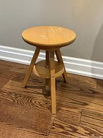Full view of round wooden adjustable stool showing seat, central screw column, legs, and shelf