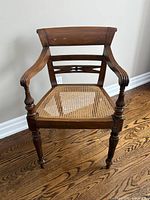 Front view of antique wood armchair showing backrest, arms, cane seat, and turned legs