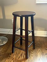 Full view of wooden bar stool showing round seat, four legs, cross-bars