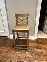 Front view of one wooden Ikea Ingolf counter chair showing X-back and seat surface