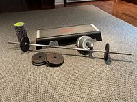 Full view of barbell with plates, Reebok step, ab wheel and foam roller