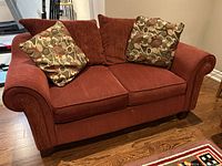 Front view of brick red loveseat with two patterned cushions