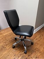 Three-quarter side view of entire chair showing black leather upholstery, chrome base and casters