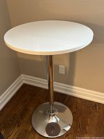 Full view showing white round top and chrome base of adjustable cocktail table