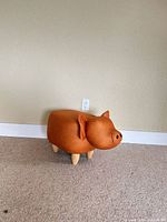 Front left view of pig-shaped ottoman showing faux leather body, ears, wood legs
