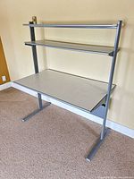 Front view of gray metal desk with two shelves and work surface
