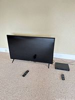 Front view of 43" LG TV on stand, Blu-ray player and two remotes on floor