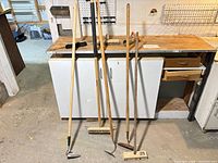 Five long-handled tools and three small items on workbench