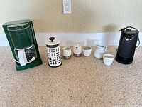 Full view of all items: green Krups coffee maker, Bodum French press, sugar bowls, creamers, black can opener